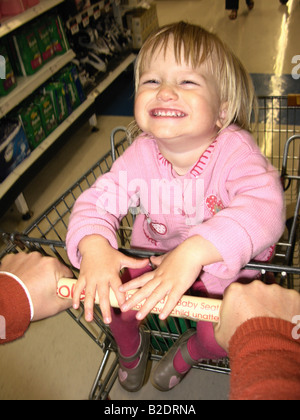 Child girl laughing and sitting in supermarket trolley Stock Photo