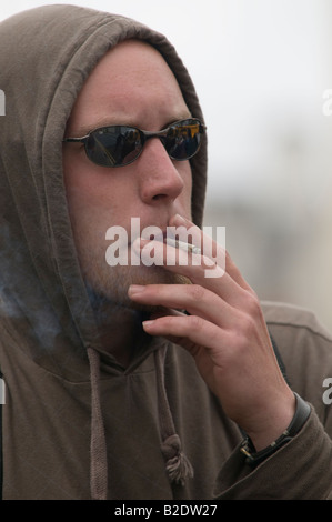 young Man wearing hoodie wearing dark glasses and smoking roll up cigarette, UK Stock Photo