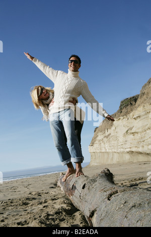 Young couple balancing on log at beach. Stock Photo