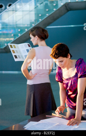 Mid adult woman making a blueprint with a young woman looking at a color swatch Stock Photo