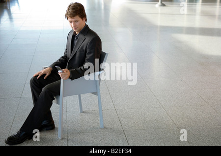 Businessman sitting in an armchair and text messaging with a mobile phone Stock Photo