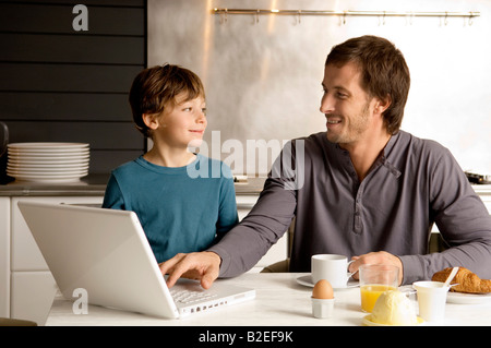Mid adult man using a laptop and looking at his son Stock Photo
