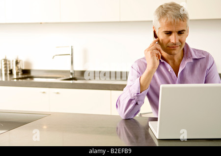 Mature man working on a laptop while talking on a mobile phone Stock Photo