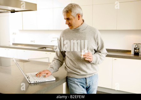 Mature man working on a laptop in the kitchen Stock Photo