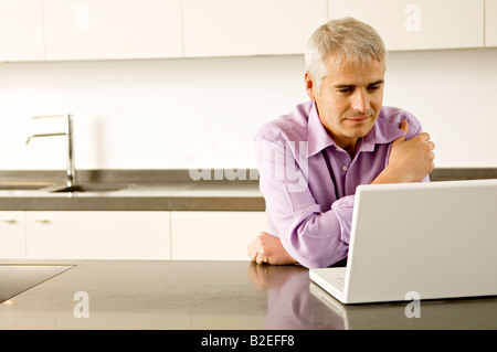Mature man using a laptop in the kitchen Stock Photo