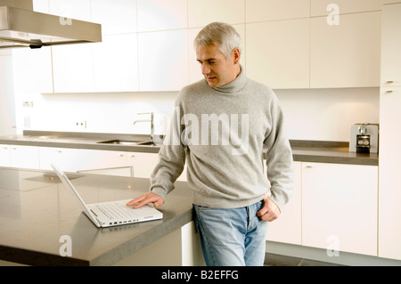 Mature man working on a laptop in the kitchen Stock Photo