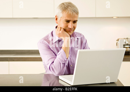 Mature man working on a laptop in the kitchen Stock Photo