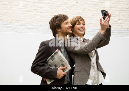 Young woman taking a picture with a digital camera and a mid adult man standing behind her Stock Photo