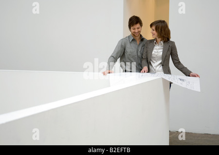 Mid adult man looking at a blueprint and smiling with a young woman standing beside him Stock Photo