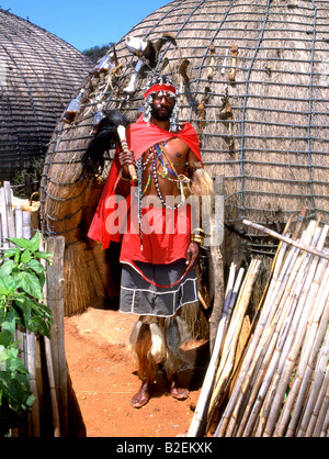 Zulu Sangoma or diviner in traditional dress in front of beehive huts