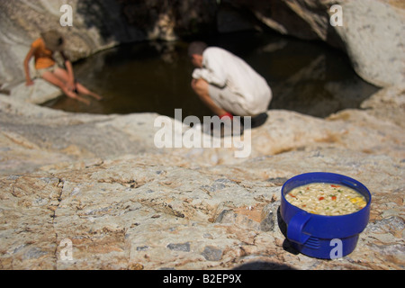 Hikers cooling down in rock pool on the Naukluft Hiking trail, cup of soup in the foreground Stock Photo