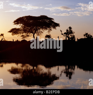 Sunset on the banks of the Omo River near a Dassanech village.  Two dome-shaped granaries are just visible in the trees. Stock Photo