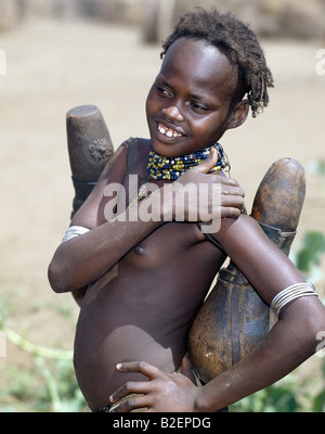 A young Dassanech girl carrying wooden milk containers.  Milk containers are regularly sterilized with smoke from aromatic wood. Stock Photo