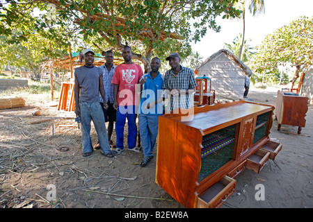 A group of cabinet makers pose next to a completed crockery cabinet in an outdoor furniture factory in rural Mozambique Stock Photo