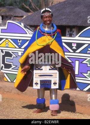 Ndebele Woman in traditional dress standing in front of traditionally painted house Stock Photo