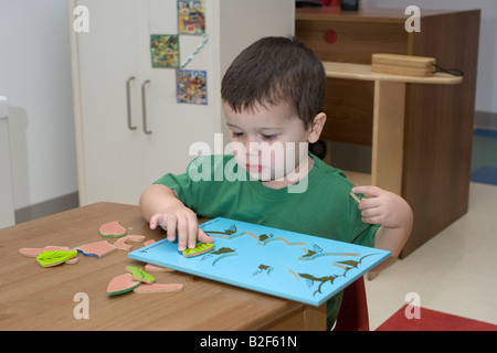 4 year old pre school boy sitting at a table doing a puzzle Stock Photo