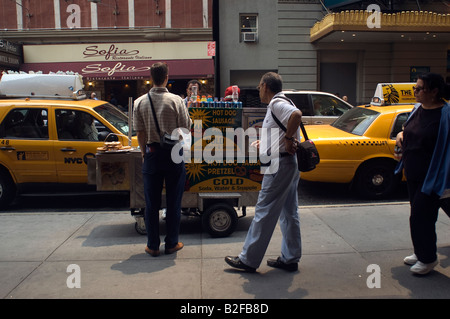 Tourists buy frankfurters and pretzels from a Hot Dog vendor in the theater district in New York NY Stock Photo