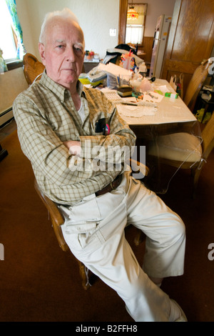 A senior gentleman sits in a chair in his messy dining room Stock Photo
