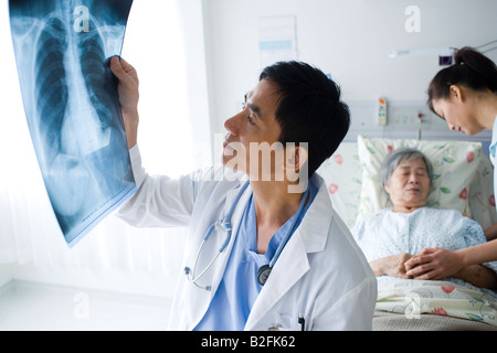 Male doctor examining at an X-Ray report with two women in the background Stock Photo