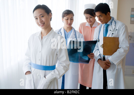 Portrait of a female nurse smiling with other doctors examining an X-Ray report in the background Stock Photo