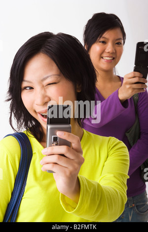 Two young women using mobile phones and smiling Stock Photo