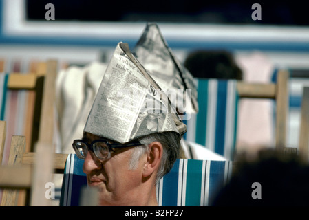 man wearing a newspaper hat sitting on deckchair Stock Photo