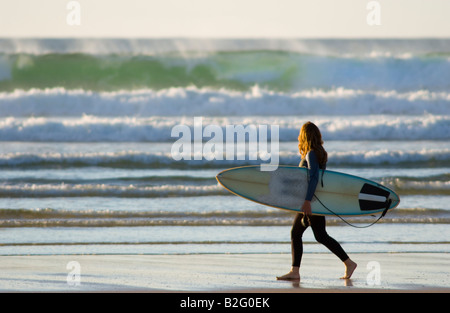 Atmospheric images of surfers walking along surf and beach with surfboard during a warm summer on the Cornish coast in England Stock Photo