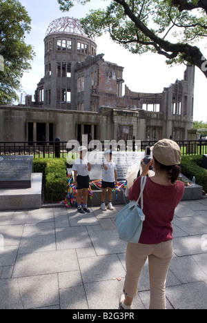 A woman takes a photo of her kids posing in front of the A-bomb dome memorial in Hiroshima Peace Park Stock Photo