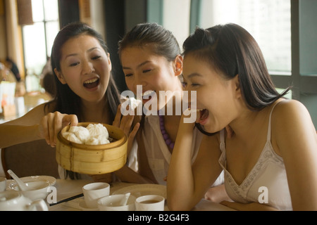 Young woman offering Chinese dumpling to her friends and laughing Stock Photo