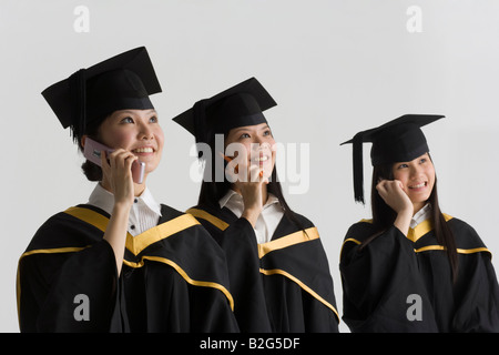 Three young female graduates talking on mobile phones and smiling Stock Photo