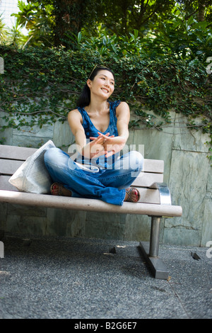 Young woman sitting on a bench in a park and stretching arms Stock Photo