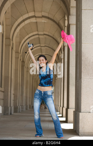 Young woman holding a home video camera and a sun hat with her arms raised Stock Photo
