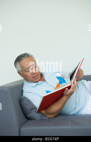 Senior man lying on a couch and reading a book Stock Photo