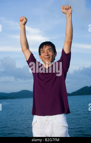 Close-up of a mid adult man standing with his arms raised and smiling Stock Photo