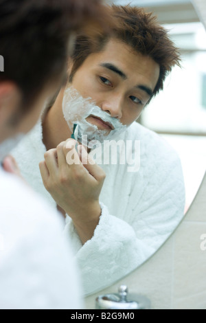 Young man shaving with a razor in the bathroom Stock Photo
