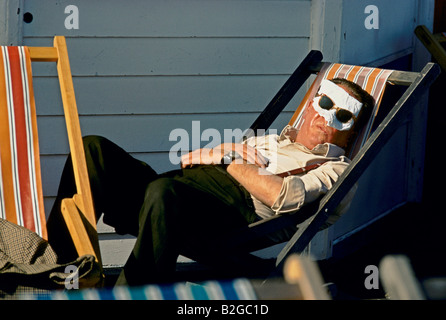 man asleep in a deckchair with his face covered by a handkerchief held on with his sunglasses Stock Photo