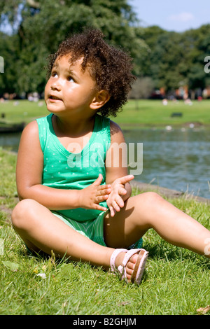 Young mixed race 4yr old girl sitting in the park on a summers day Stock Photo
