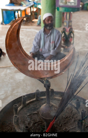 A Muslim man sits behind smoking incense sticks at a mosque near to Mysore. The cresent moon can be seen. Stock Photo