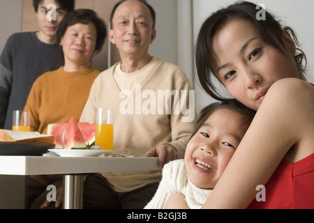 Portrait of a young woman hugging her daughter with her family members at a breakfast table