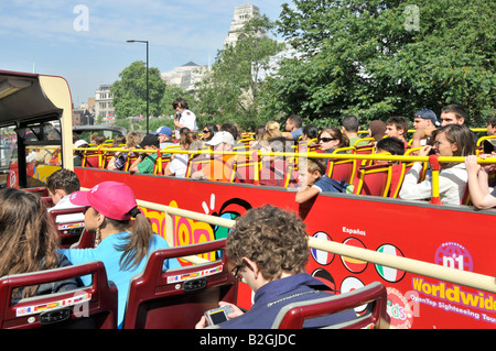 Tower Hill London two busy open top tour buses alongside each other younger tourists sightseeing from the top deck on a blue sky sunny day England UK Stock Photo