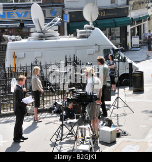 Across road from Royal Courts of Justice Law Courts journalists & reporters with TV camera crews file news reports beside satellite dish van London UK Stock Photo