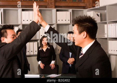 Side profile of two businessmen giving high-five with their colleagues standing behind them Stock Photo