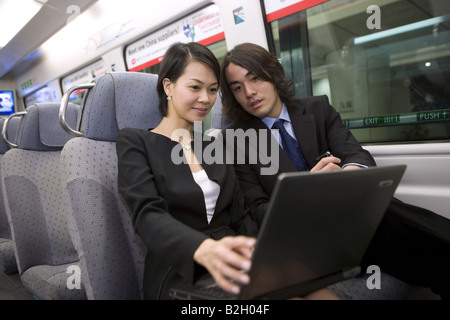 Businesswoman with a businessman using a laptop in a train Stock Photo