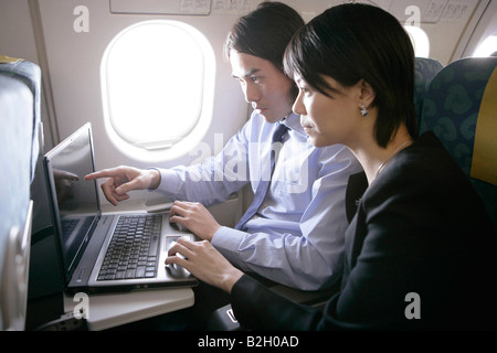 Businessman with a businesswoman using a laptop in an airplane Stock Photo