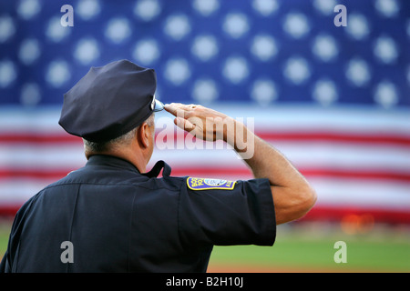 Police officer salutes giant flag baseball Fenway Park Stock Photo