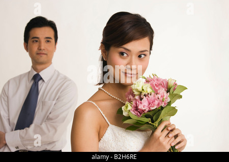 Close-up of a bride holding a bouquet of flowers with a groom standing behind her Stock Photo