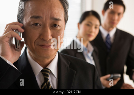Businessman using a mobile phone with his two colleagues standing behind him Stock Photo
