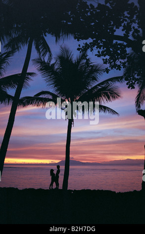 Philippines. Silhouette of young couple leaning against palm tree on the beach at sundown. Stock Photo