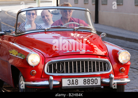 Old classic model of red convertible Czech Skoda with tourists and driver on a sightseeing tour of the old quarters of Prague Stock Photo