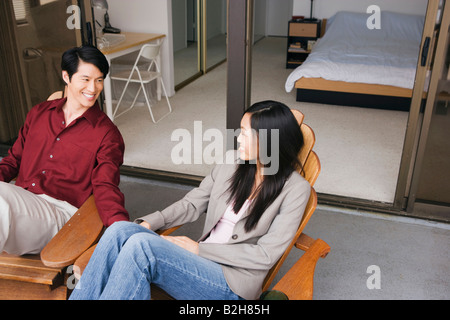 Young couple sitting on chairs looking at each other and smiling Stock Photo